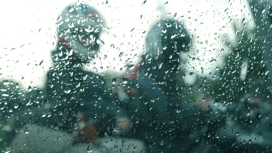 Image of rain drops on glass with faded motorcyclists in the background