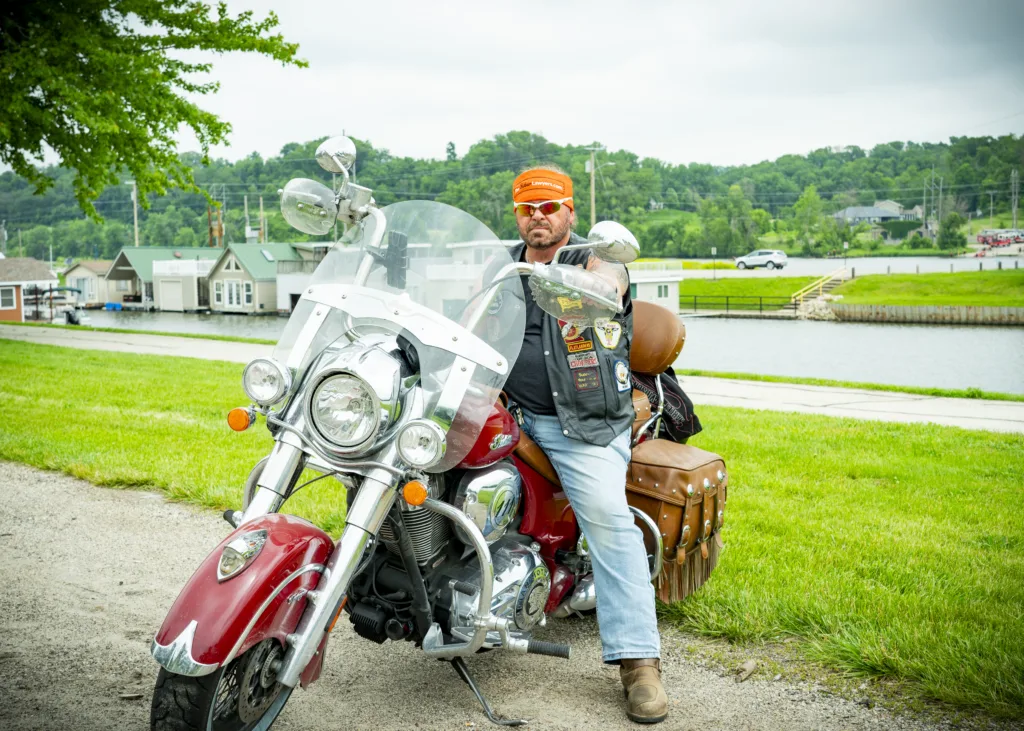 Iowa Personal Injury Attorney Pete Leehey of The Biker Lawyers sits on his red motorcycle next to a river