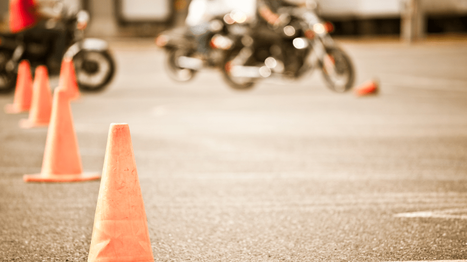 Image of cones in a parking lot with motorcycles practicing basic meneuvers in the background