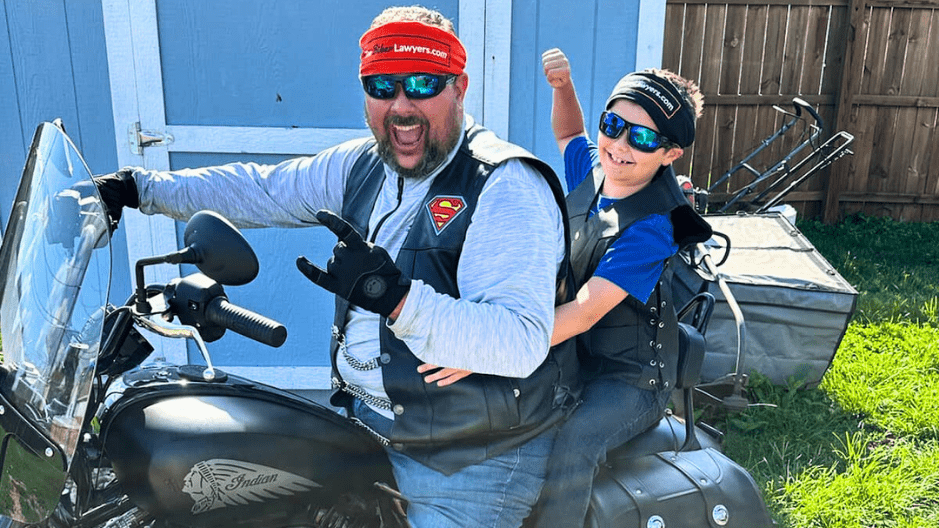 Steven Adelmund, Director of Marketing for The Biker Lawyers, sits on his Indian Bobber Chief Dark Horse Motorcycle with his son.