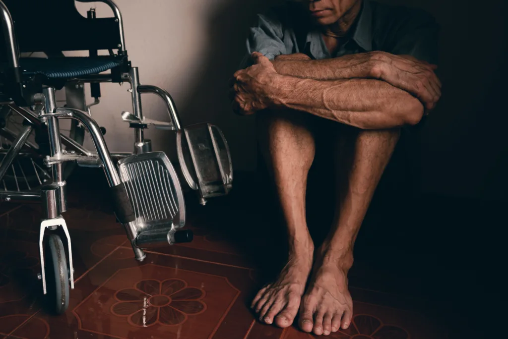 Image of a man sitting on a floor next to a wheelchair