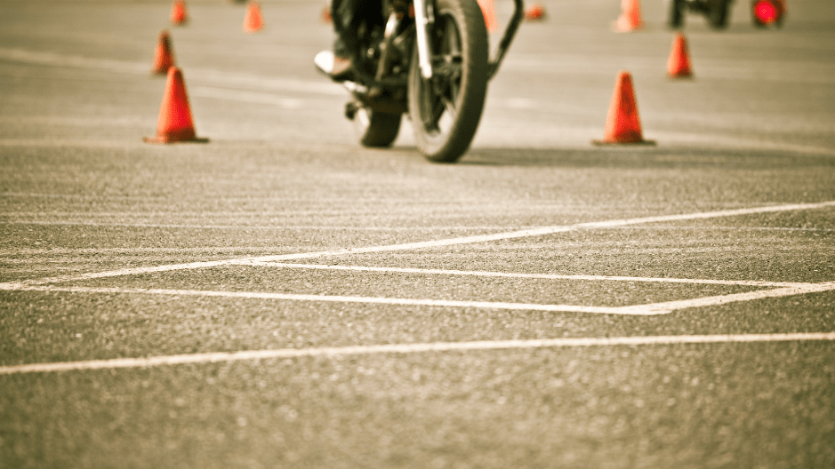 A motorcyclist practices weaving between cones in a parking lot