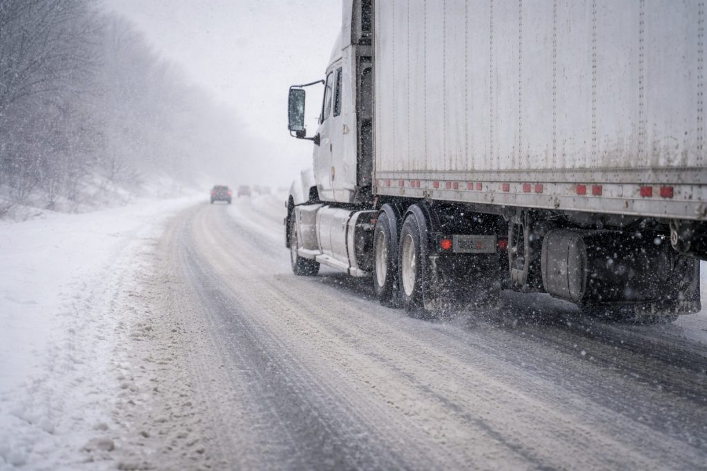 Close-up side view of a semi-truck driving cautiously on a snowy highway in Iowa